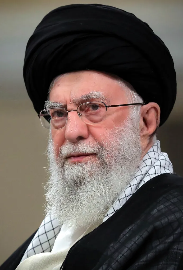 Supreme Leader Ayatollah Ali Khamenei, wearing a black turban, glasses, and a white patterned scarf, looks forward with a serious expression.