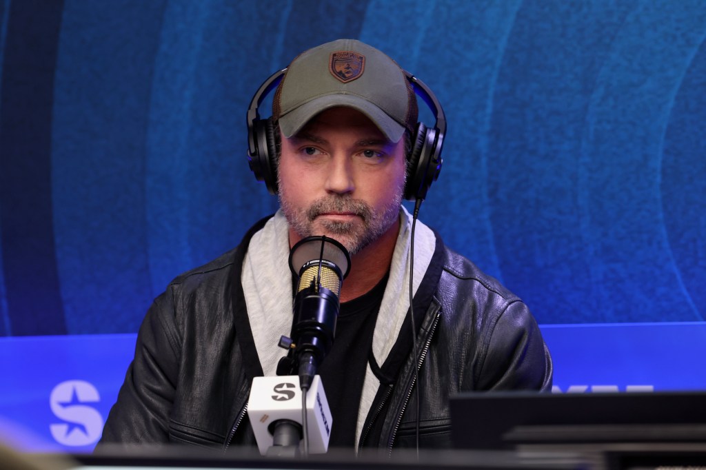 Aaron Phypers in a studio wearing headphones and speaking into a microphone.