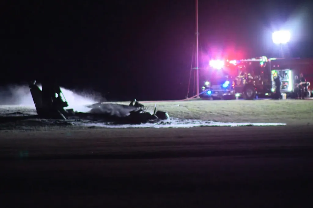 Firefighters spraying foam on a crashed plane at night.