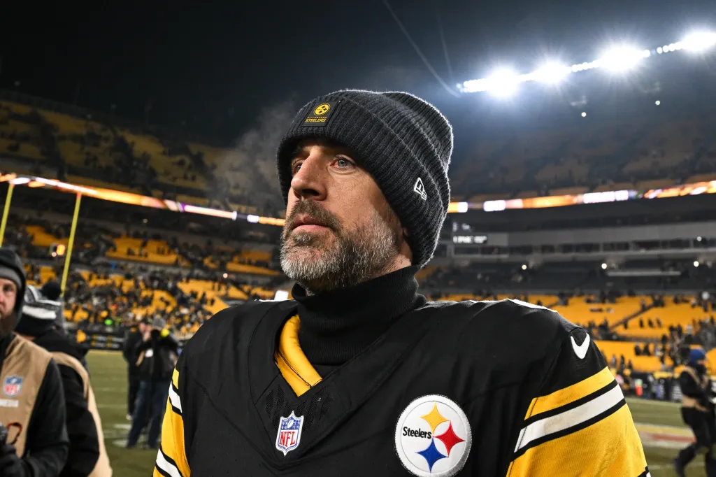 Aaron Rodgers wearing a Pittsburgh Steelers uniform and beanie, looking out over a stadium at night.