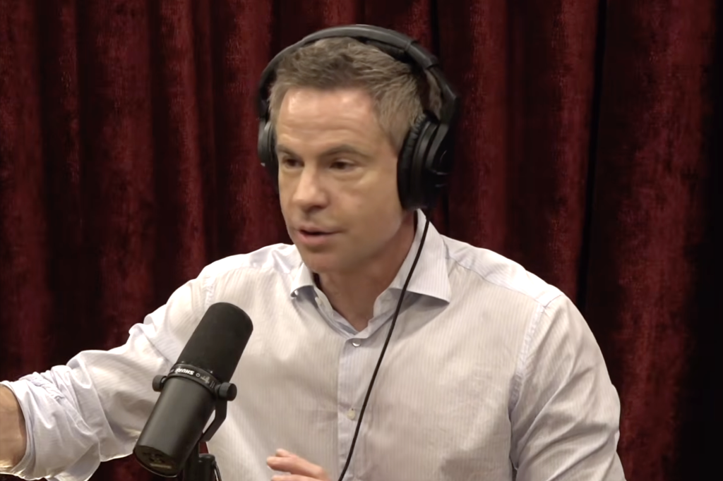 Joe Rogan wearing headphones and speaking into a microphone.