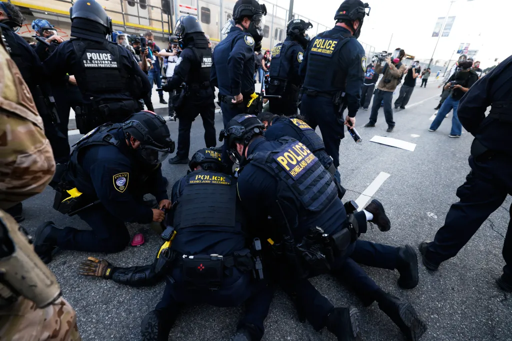 Police officers detain a protestor on the ground during a