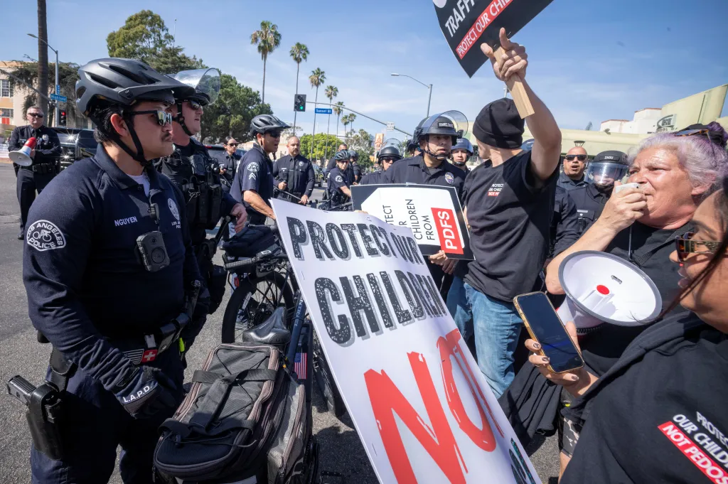 Police officers stand guard as demonstrators protest with signs and megaphones outside the Academy Awards venue.