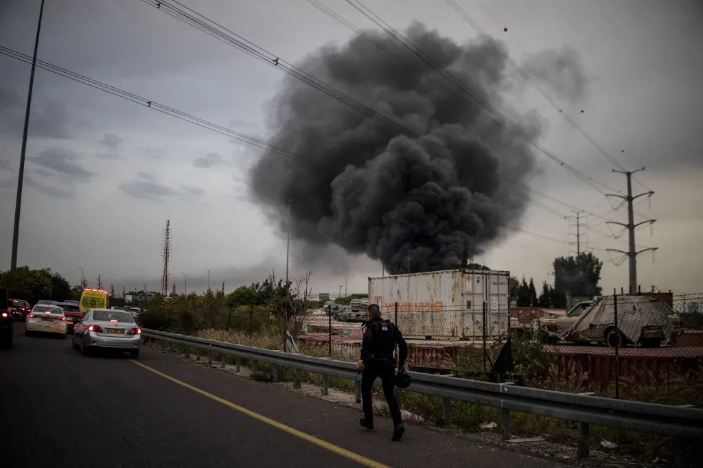 A policeman runs towards a large plume of black smoke rising from an impact site in central Israel.