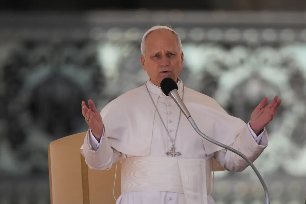 Pope Leo XIV in white robes with his hands out speaking into a microphone