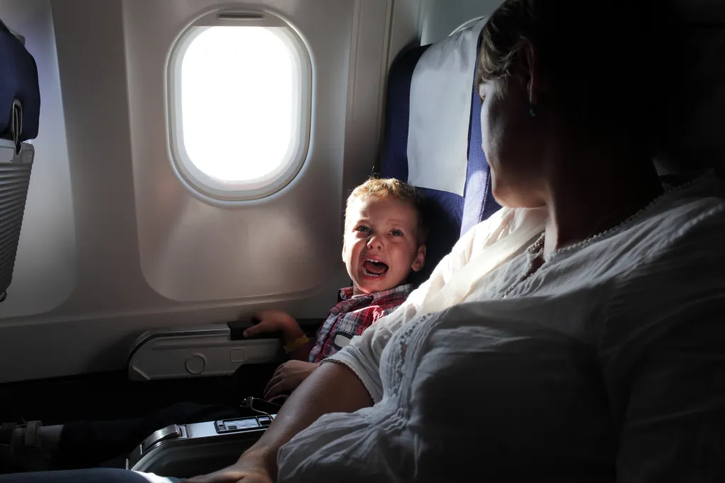 A crying boy sits next to an adult woman on an airplane.