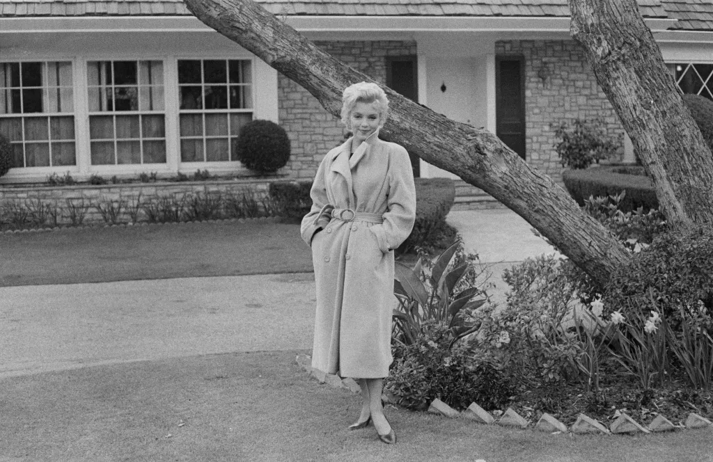 Marilyn Monroe posing outside her home in a long coat.