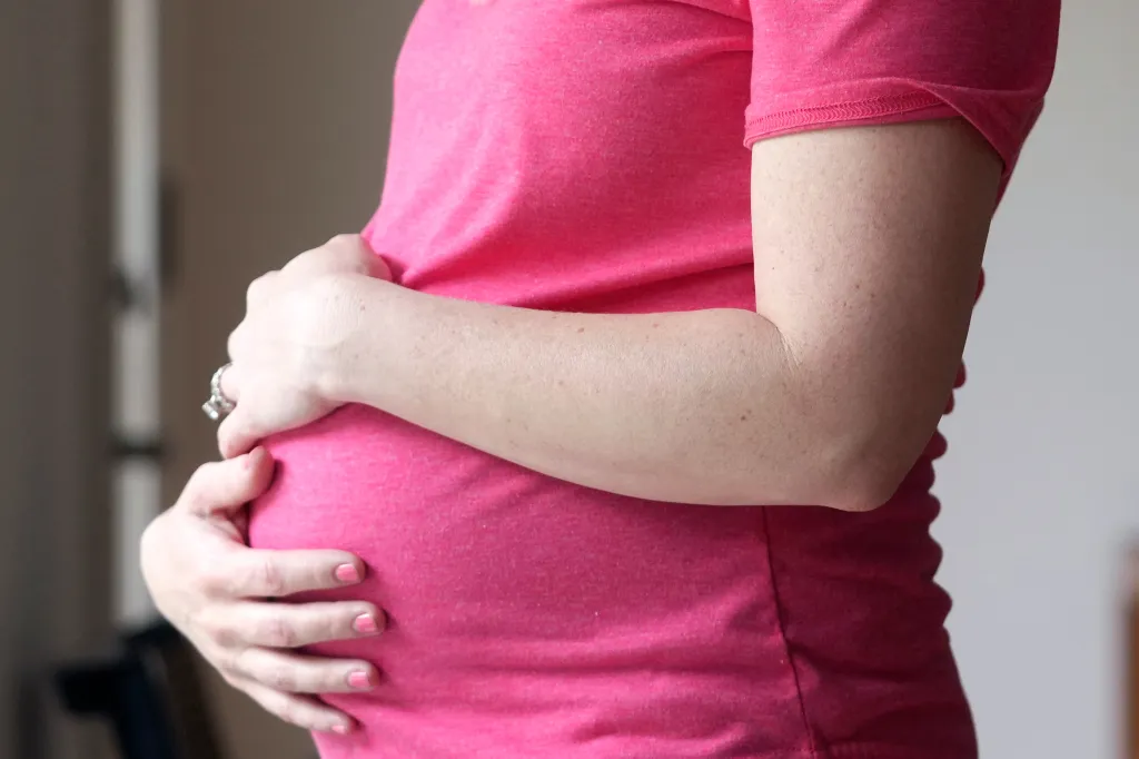 A pregnant woman wearing a pink shirt holds her belly.