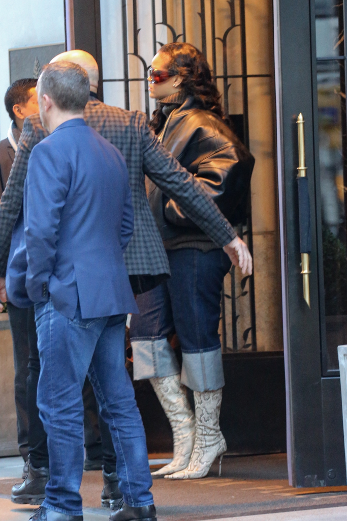 Rihanna in a black leather jacket, turtleneck, and snakeskin boots walks with A$AP Rocky and security personnel.