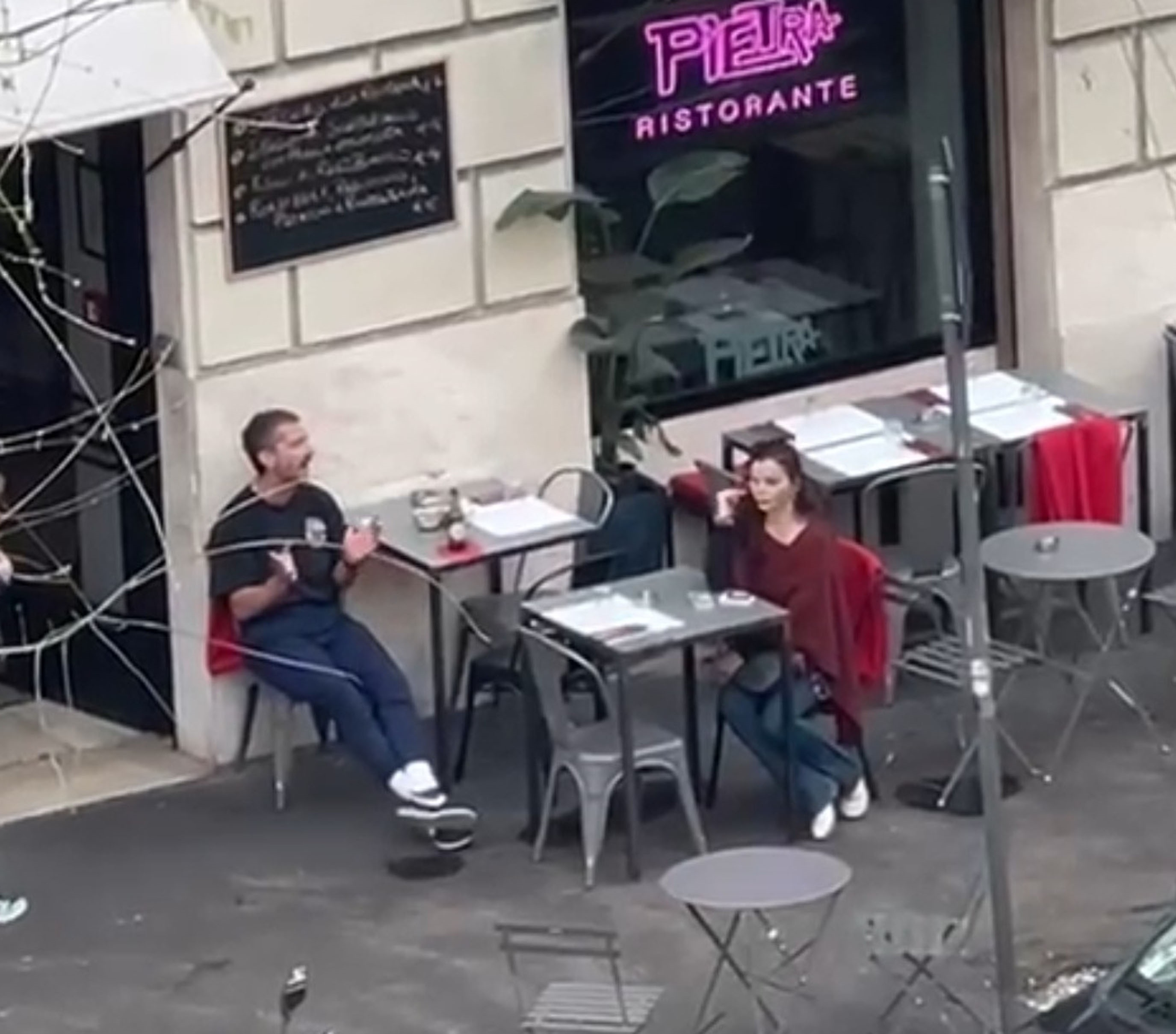Shia LaBeouf animatedly speaks to a woman seated across from him at an outdoor restaurant in Rome.