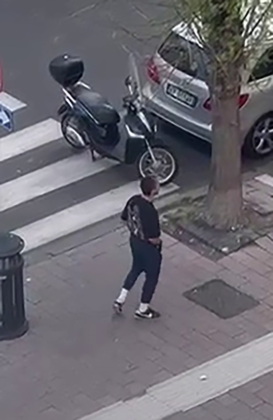 Shia LaBeouf walking on a sidewalk next to parked vehicles in Rome.