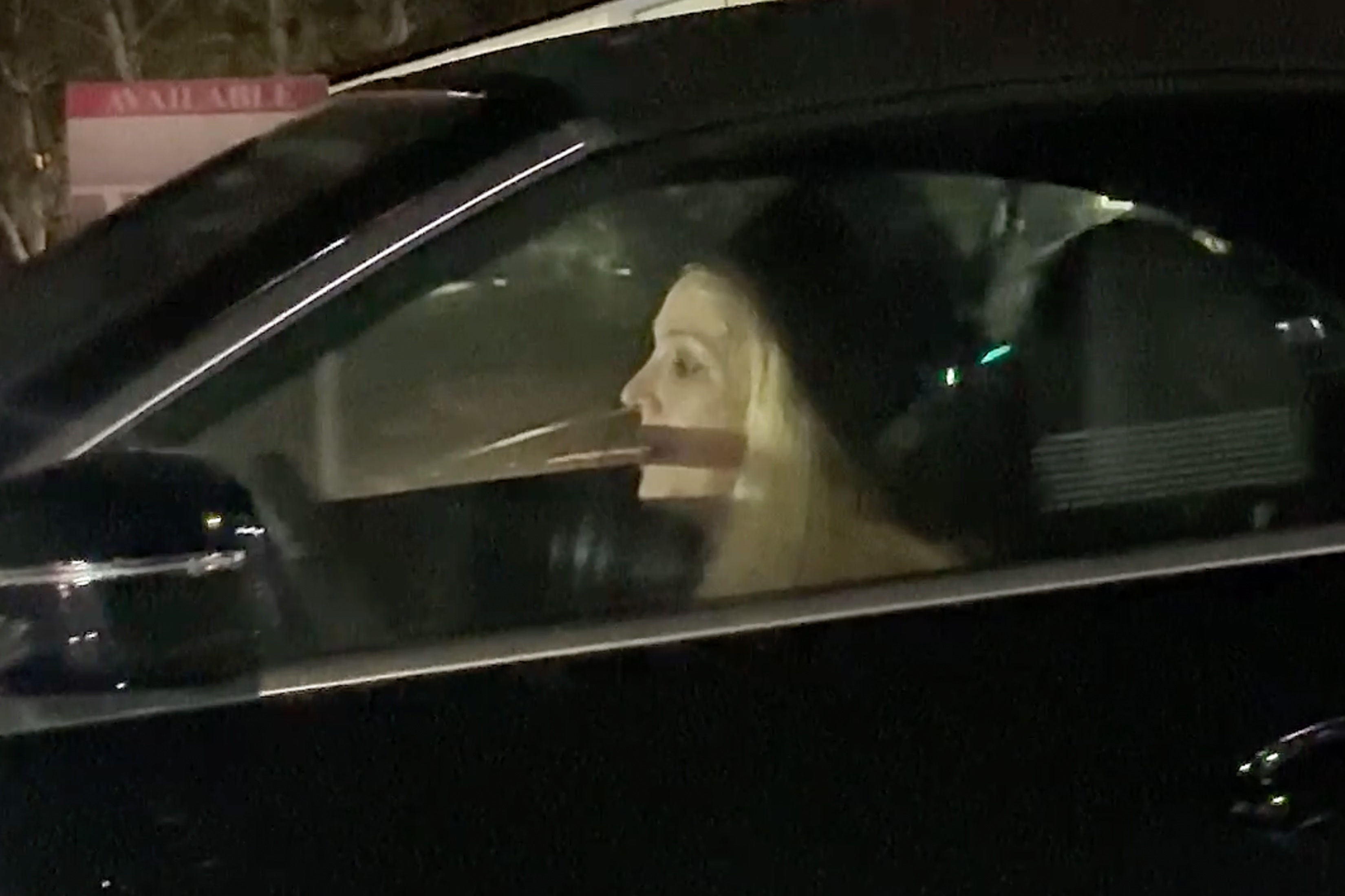 Britney Spears in the driver's seat of a black convertible BMW, looking out the window.