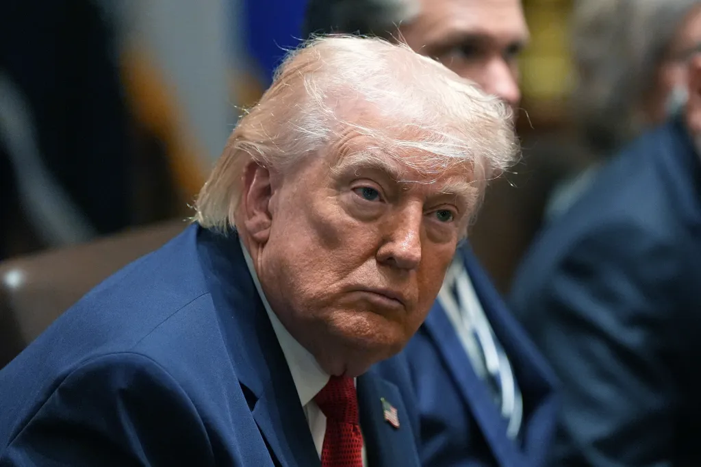President Donald Trump in a dark suit and red tie looking forward during a meeting.