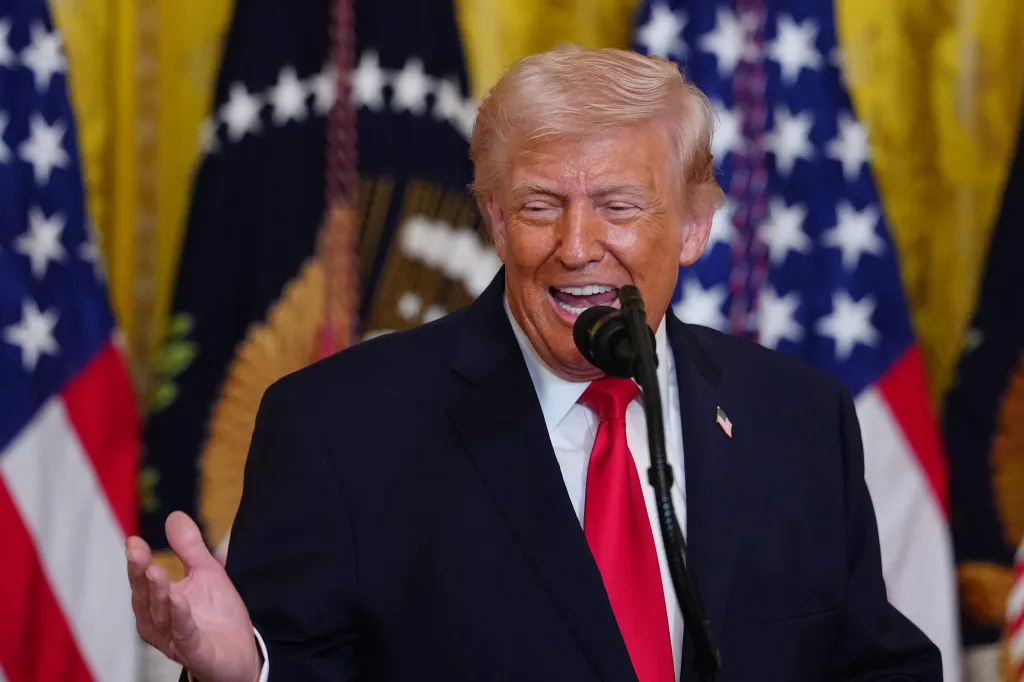 Donald Trump speaking at a Women's History Month event, with his mouth open and right hand raised.