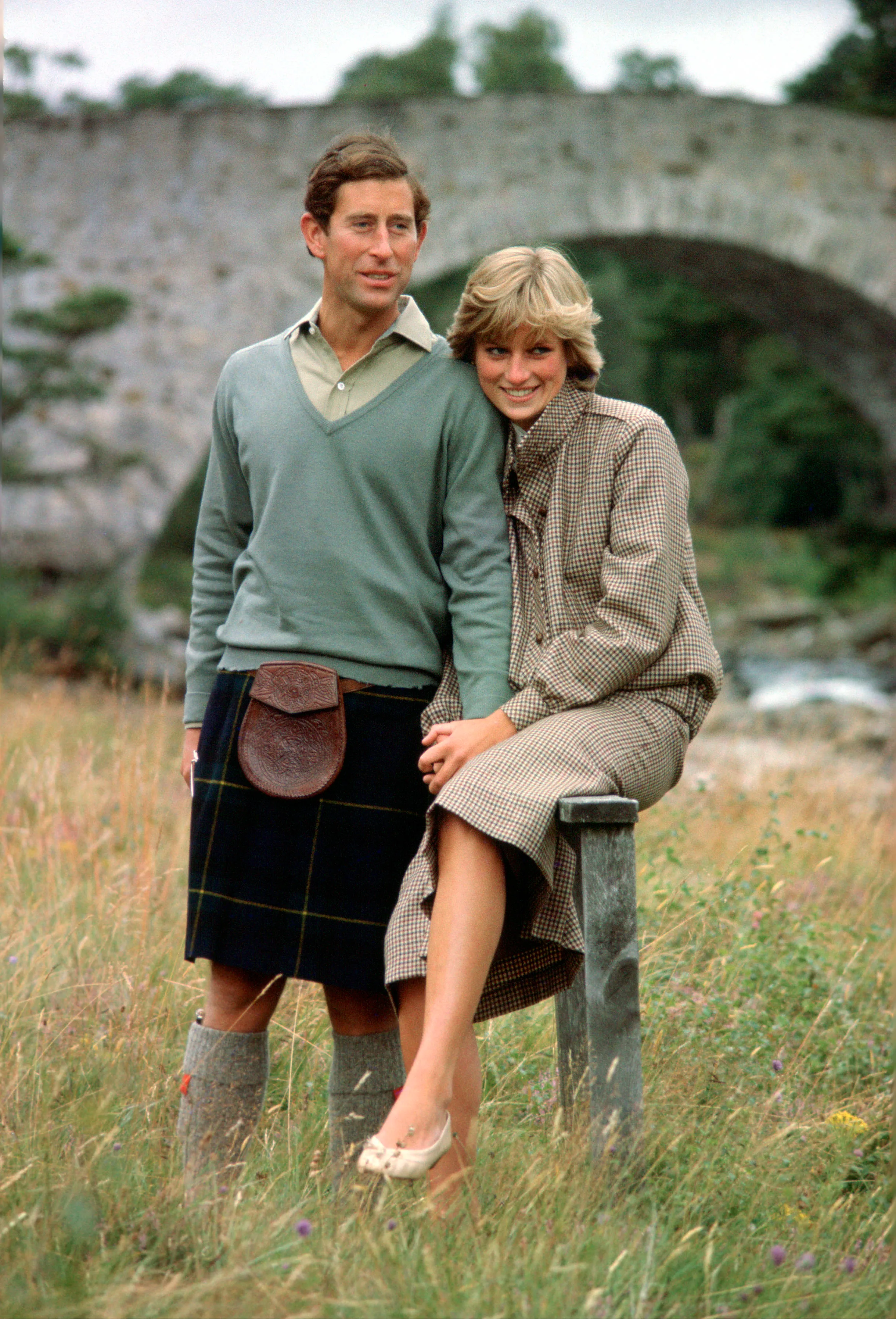 Prince Charles in a kilt and Princess Diana in a tweed suit smile and hold hands by the River Dee in Scotland during their honeymoon.