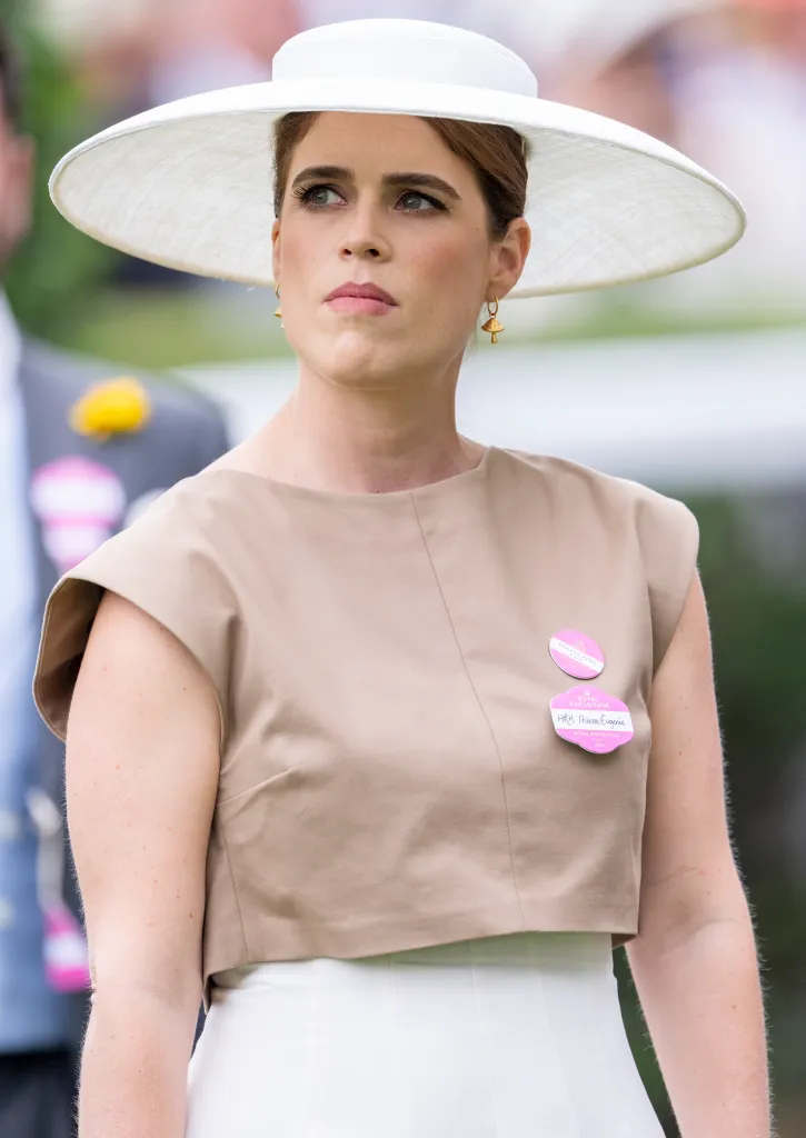 Princess Eugenie of York wearing a white wide-brimmed hat and beige top.