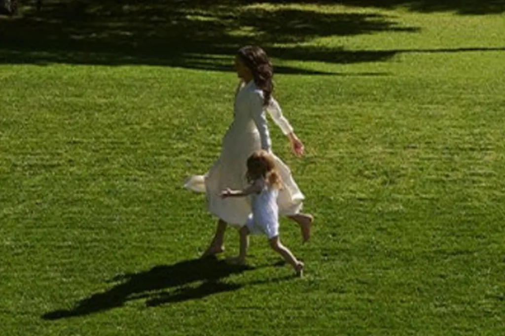 Meghan Markle and Princess Lilibet walk hand-in-hand across a grassy field.