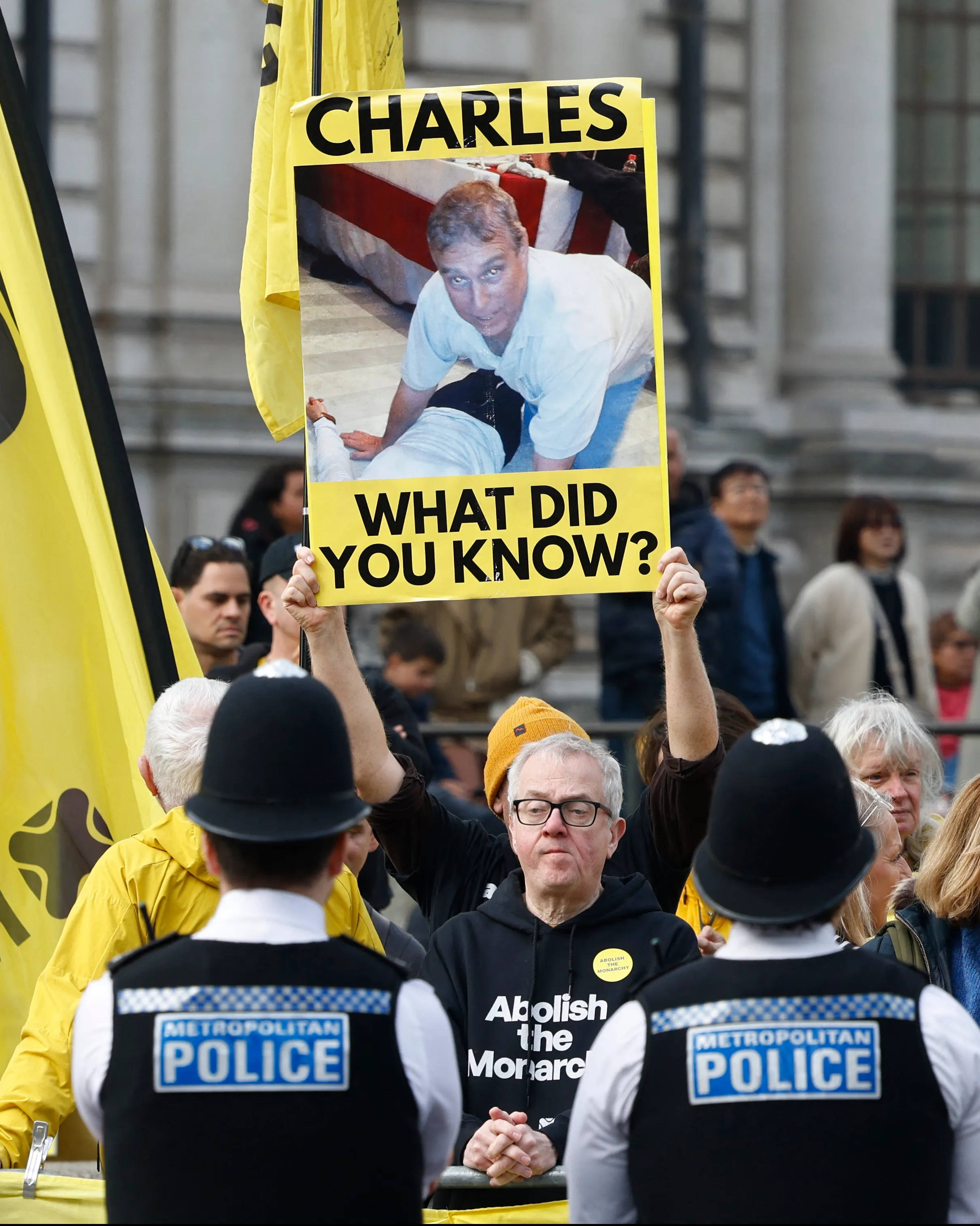 A protester holds a yellow sign featuring a picture of Prince Andrew and the text 