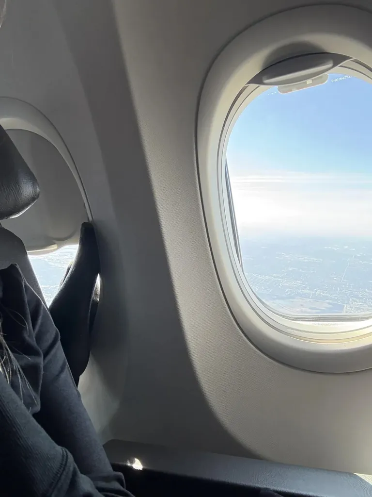 Passenger's foot on an airplane armrest near a window looking out at the sky.