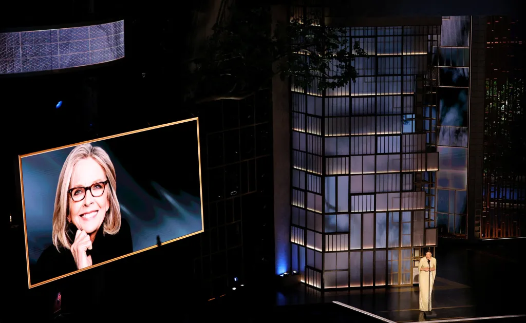 Rachel McAdams speaking at the Oscars with an image of Diane Keaton on a screen during the In Memoriam segment.