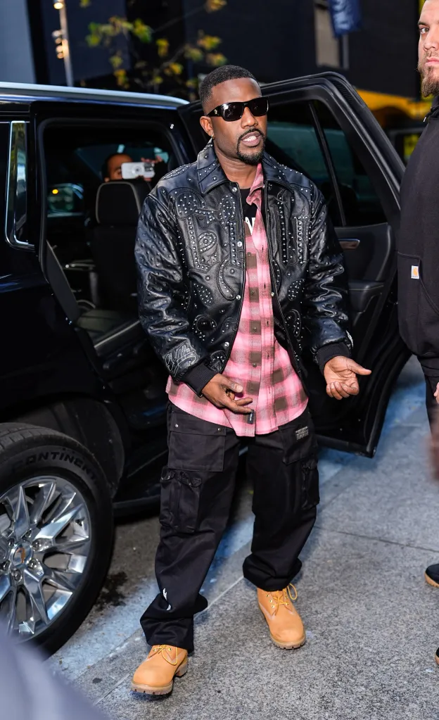 Ray J getting out of a car in a black studded leather jacket, pink plaid shirt, black cargo pants, and tan boots.