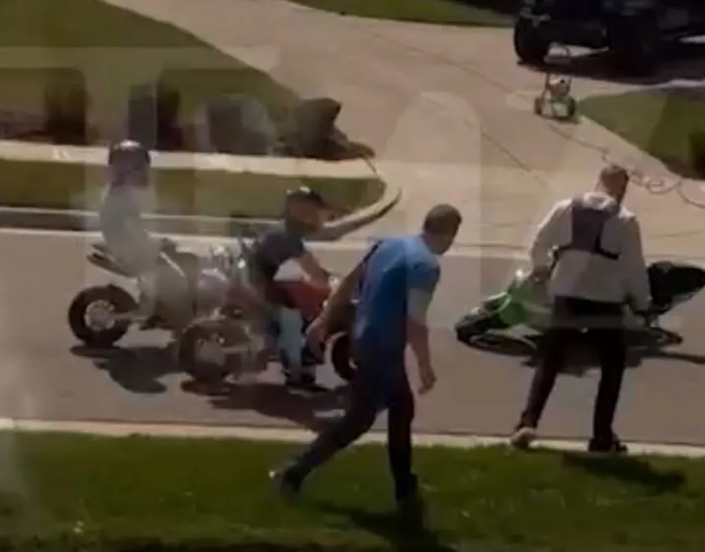 A man in a blue shirt attacking another man with a green mini-motorcycle in front of two children on other mini-motorcycles.