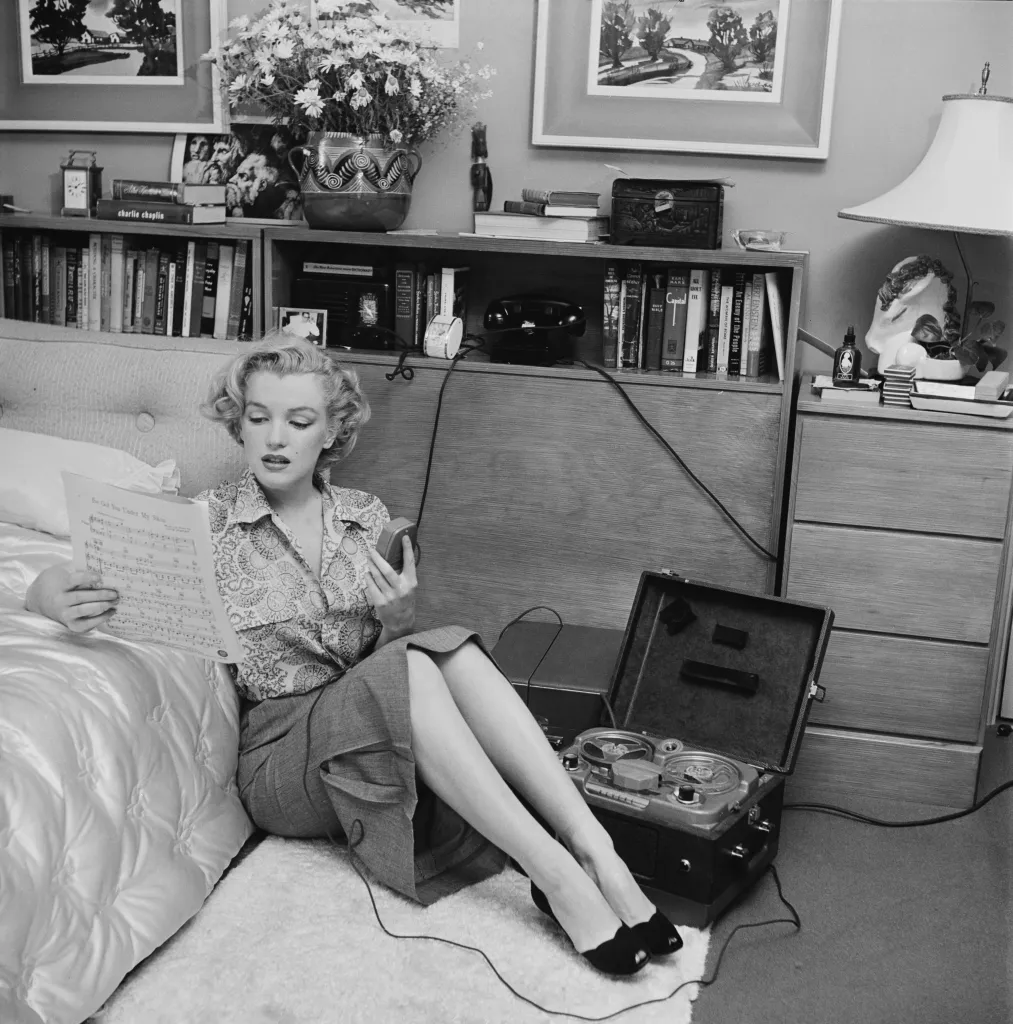 Marilyn Monroe reading sheet music while sitting on a bedroom floor with a tape player.