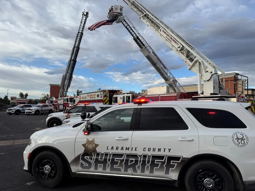 Laramie County Sheriff and Fire Department vehicles with a large American flag flying between two elevated fire truck ladders.