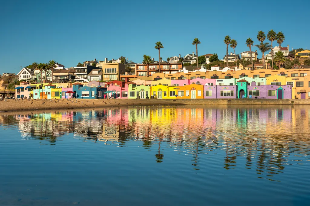 Colorful vacation homes line the shore of Capitola Village in Santa Cruz County, California, with their reflections visible in the calm water.
