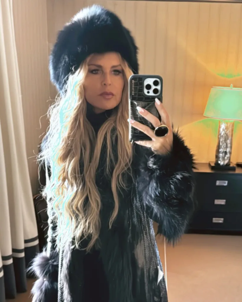 Rachel Zoe wearing a black fur hat and coat, holding a phone for a mirror selfie.