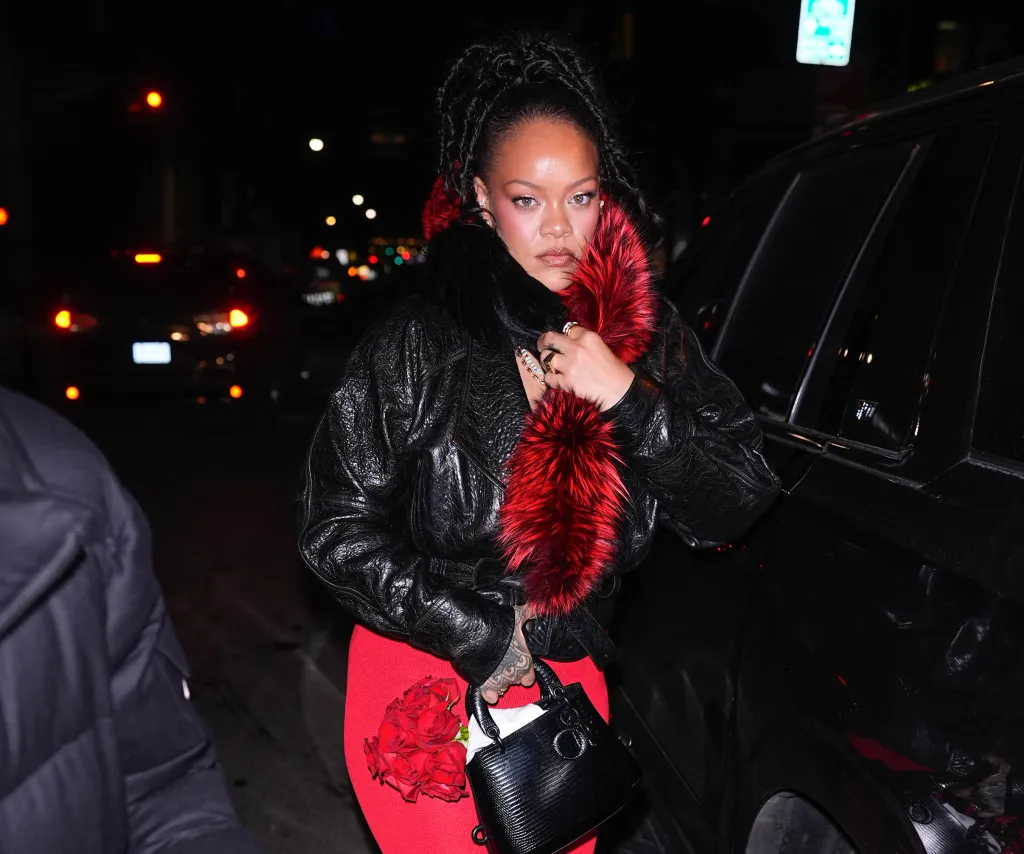 Rihanna seen in New York City wearing a black leather jacket with red fur trim, a red dress, and carrying a black purse and red roses.