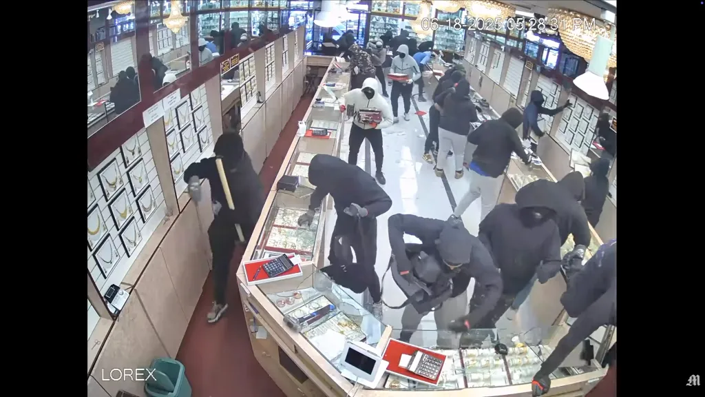 Multiple masked people smash glass display cases in a jewelry store during a robbery.