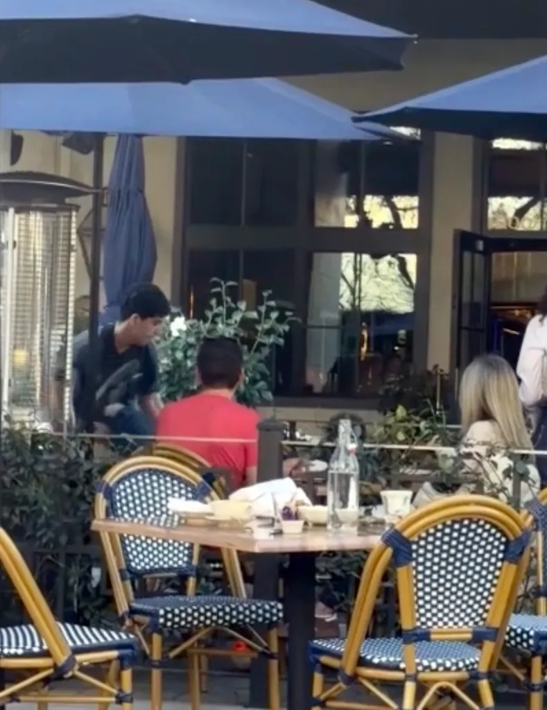People seated at an outdoor restaurant, with a person bending over in the background.