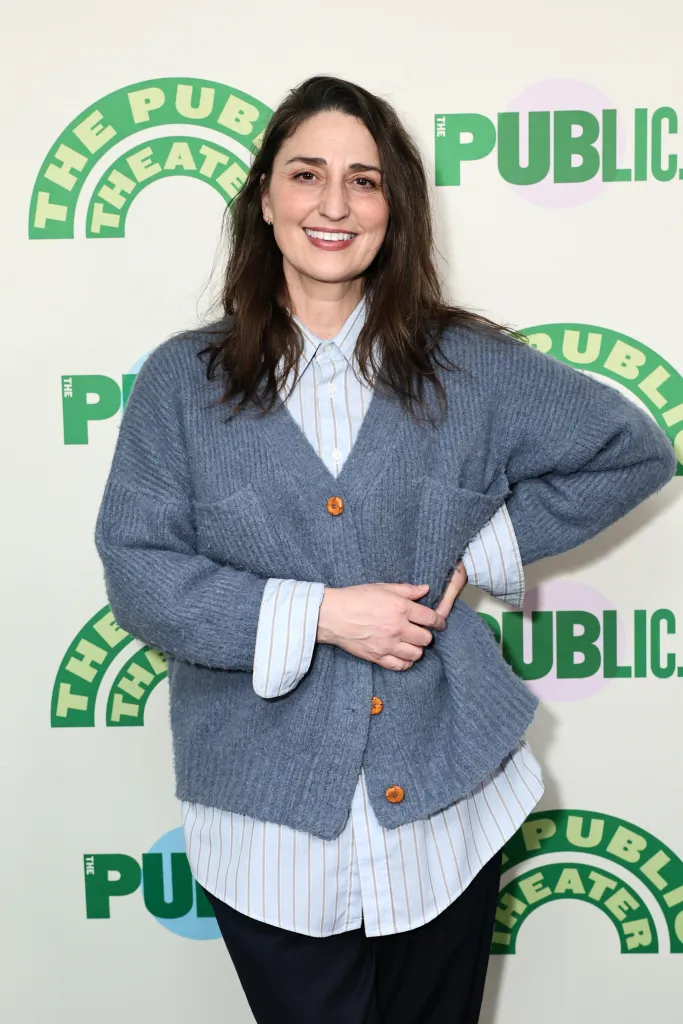 Sara Bareilles smiles in a blue cardigan over a striped shirt at the opening night of 
