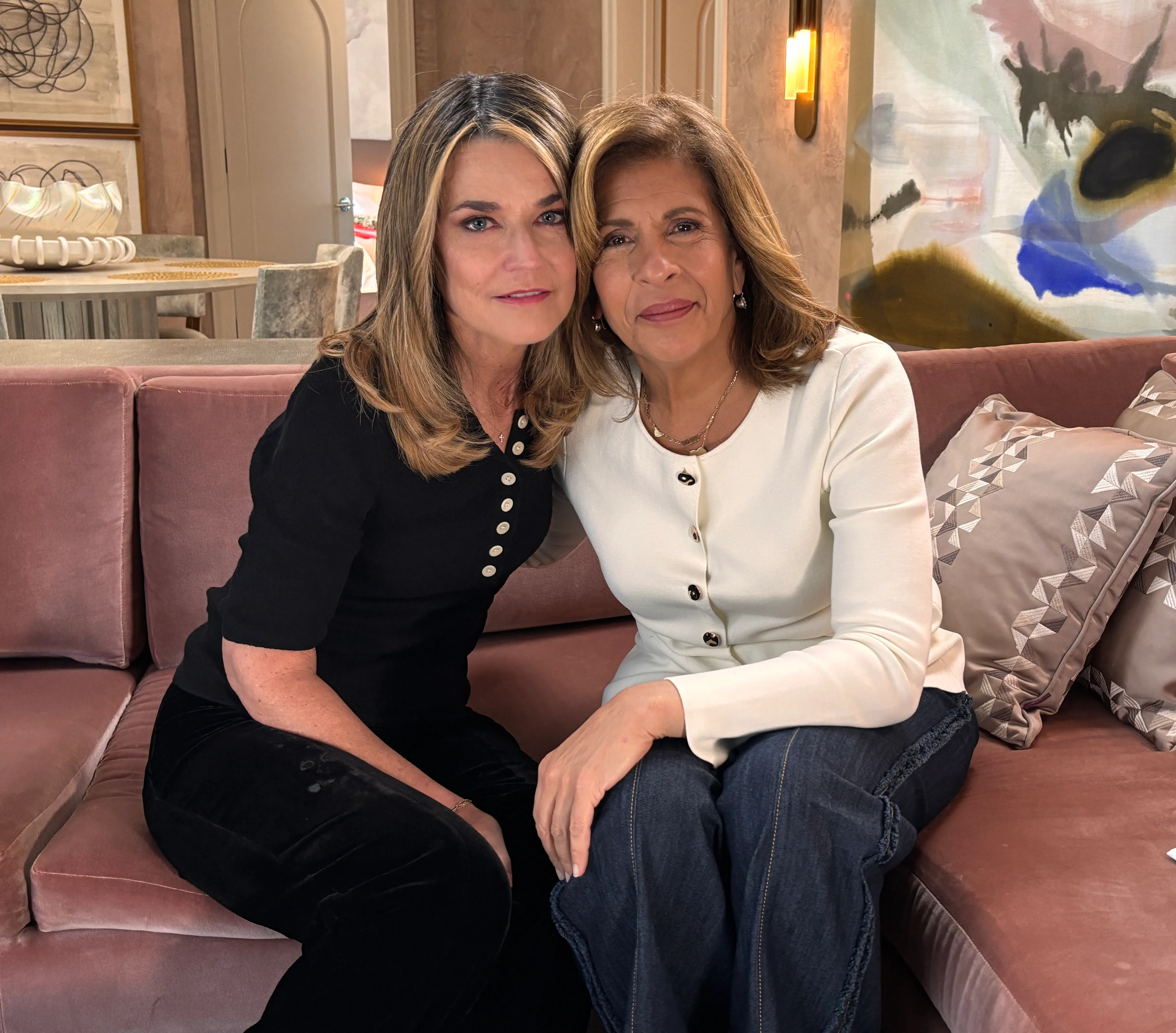 Savannah Guthrie and Hoda Kotb sitting together on a pink velvet couch.