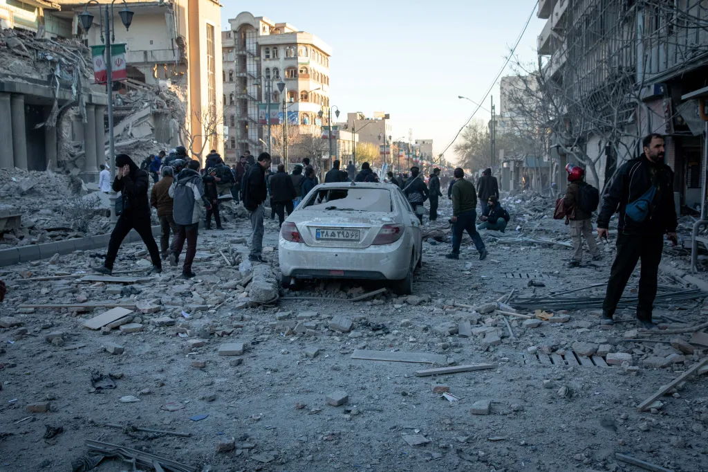 A street in Tehran covered in rubble after a US-Israeli strike, with people walking amongst the debris.