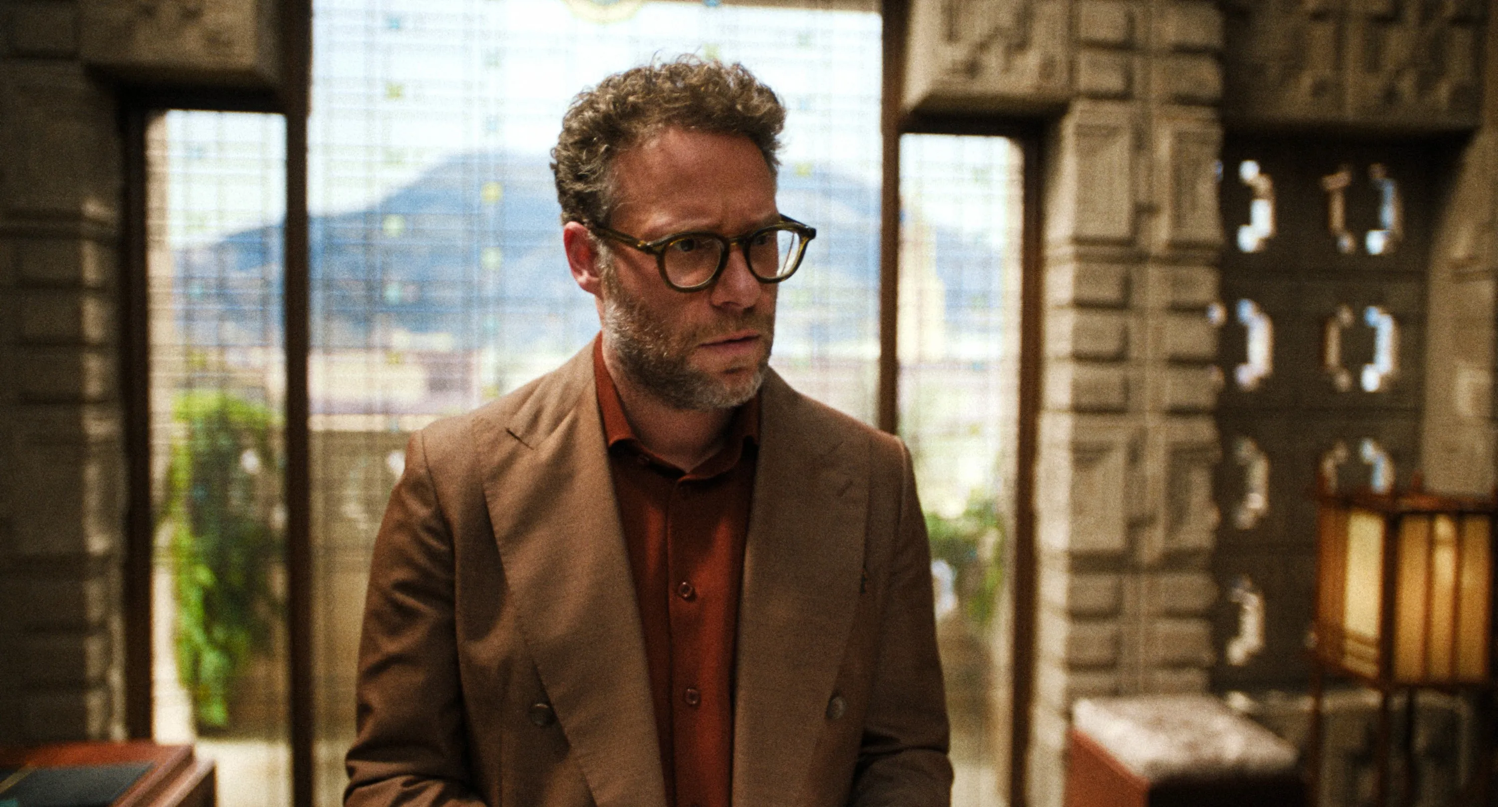 Seth Rogen in a close-up, wearing glasses and a brown suit, in 