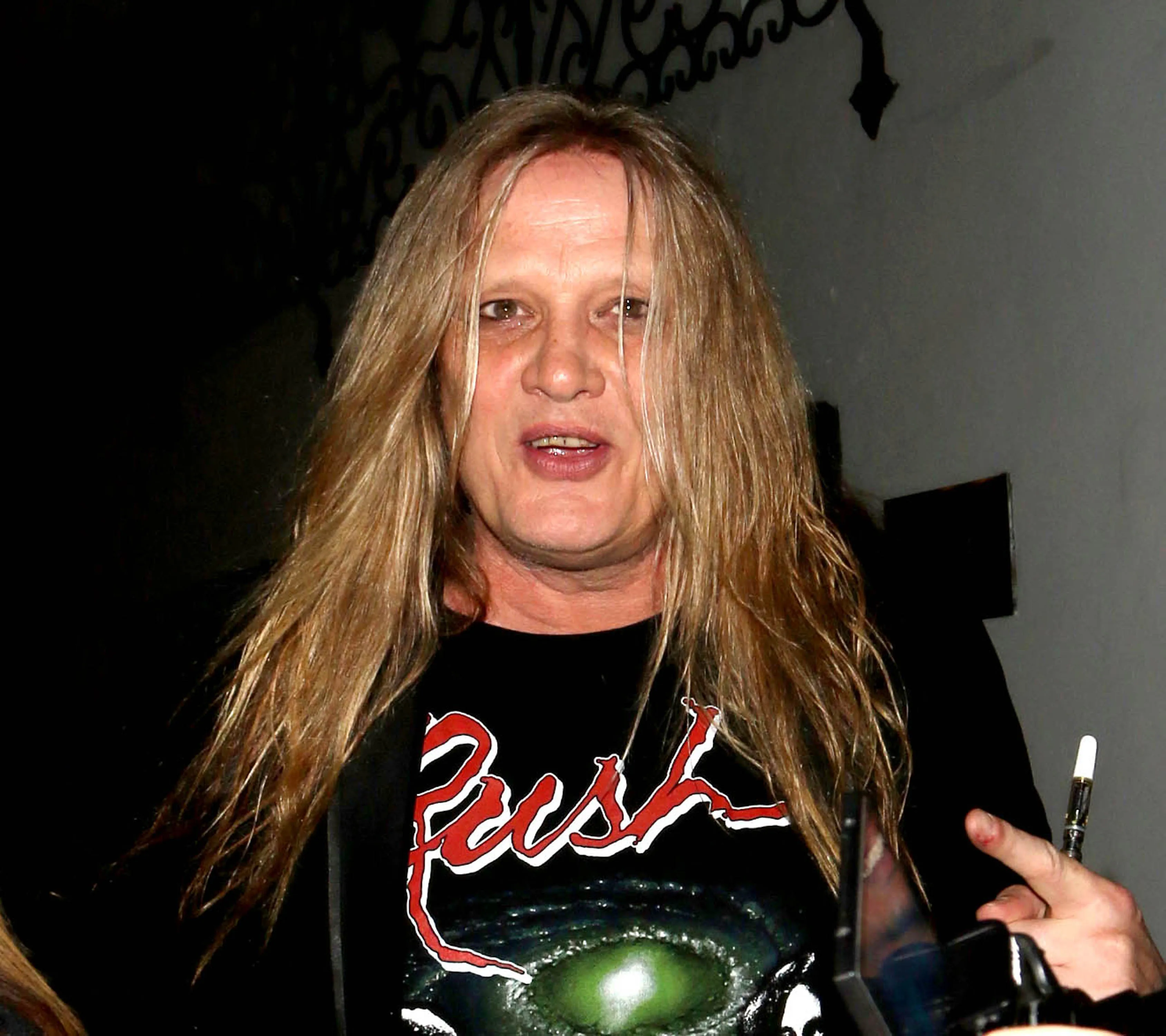Sebastian Bach, with long blonde hair, wearing a black t-shirt with the word 