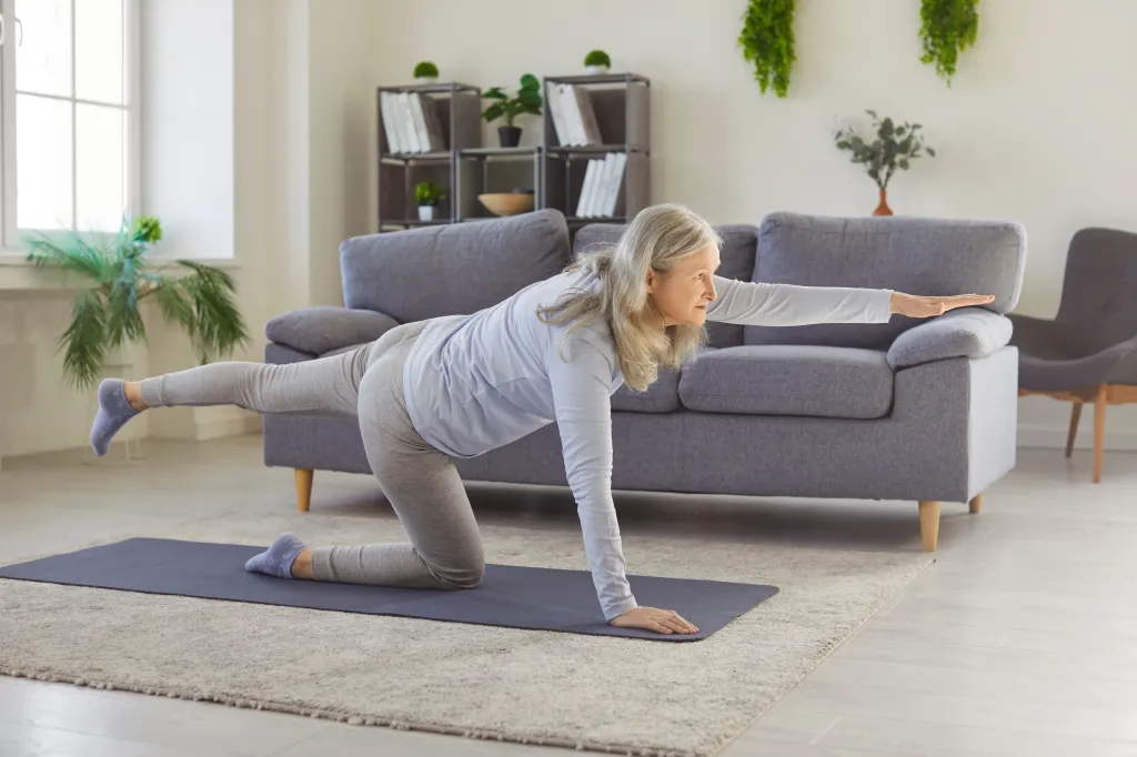 Senior woman doing a bird dog pose on a yoga mat for balance and core strength at home.
