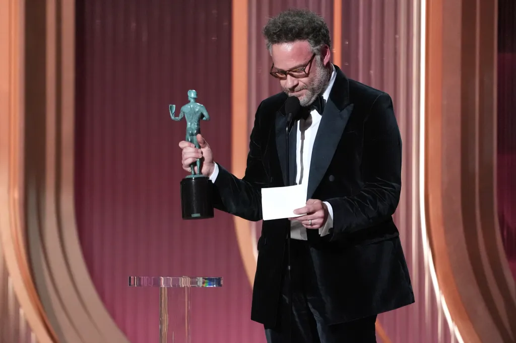 Seth Rogen holding a SAG Award and reading from a card on stage.