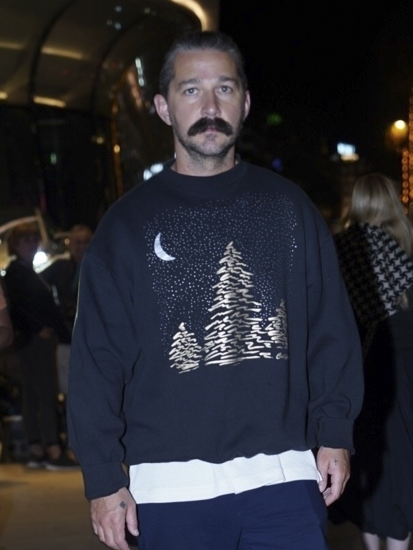 Shia LaBeouf strolling through Cannes in a black sweatshirt with a moon and trees design.