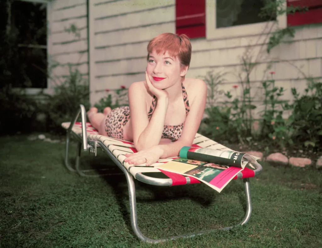 Shirley MacLaine sunbathing in a leopard print bikini on a lawn.