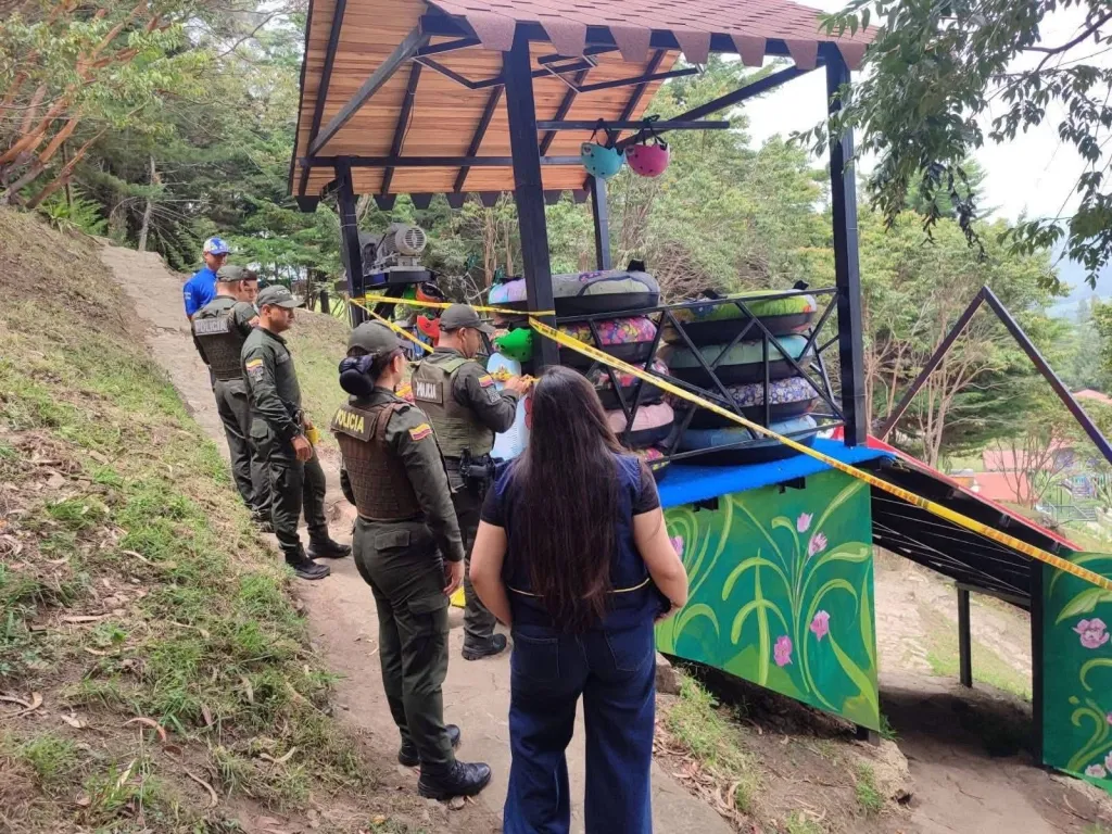 Law enforcement officers investigate a closed and taped-off amusement ride with inflatable tubes.