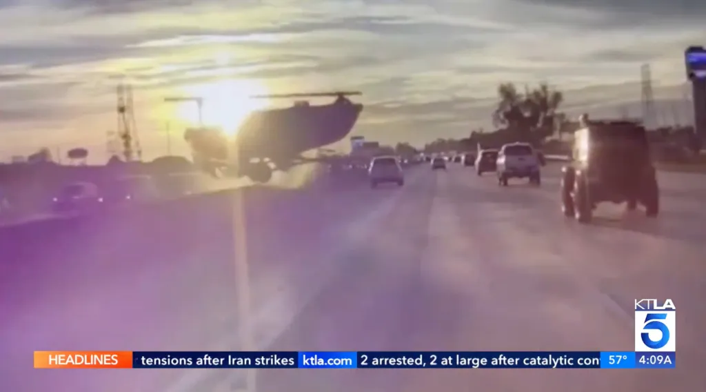 A boat flying through the air above a highway with cars driving on it.