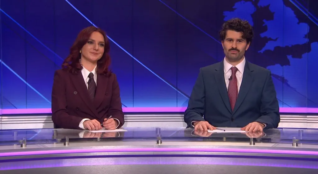 Two news anchors, a woman and a man, sit at a desk in front of a blue background with a map of the UK.