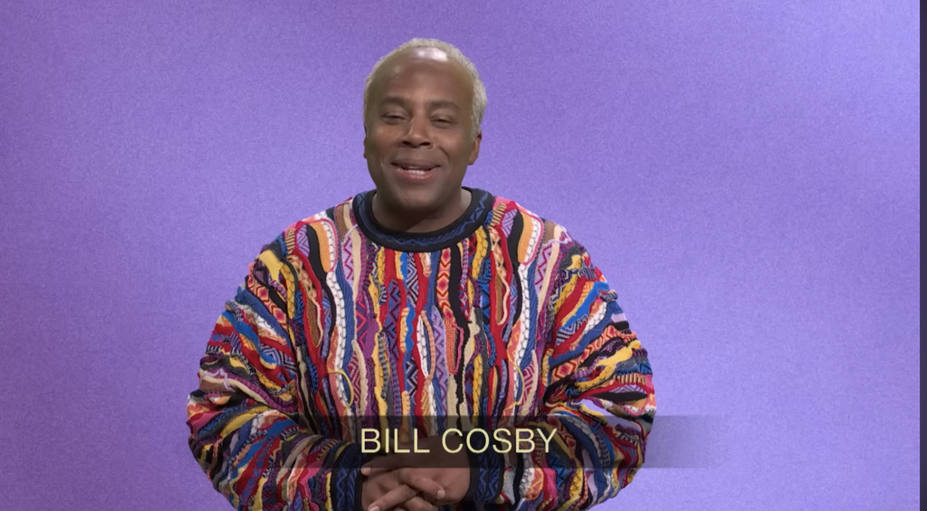 An actor dressed as Bill Cosby in a colorful sweater, with 
