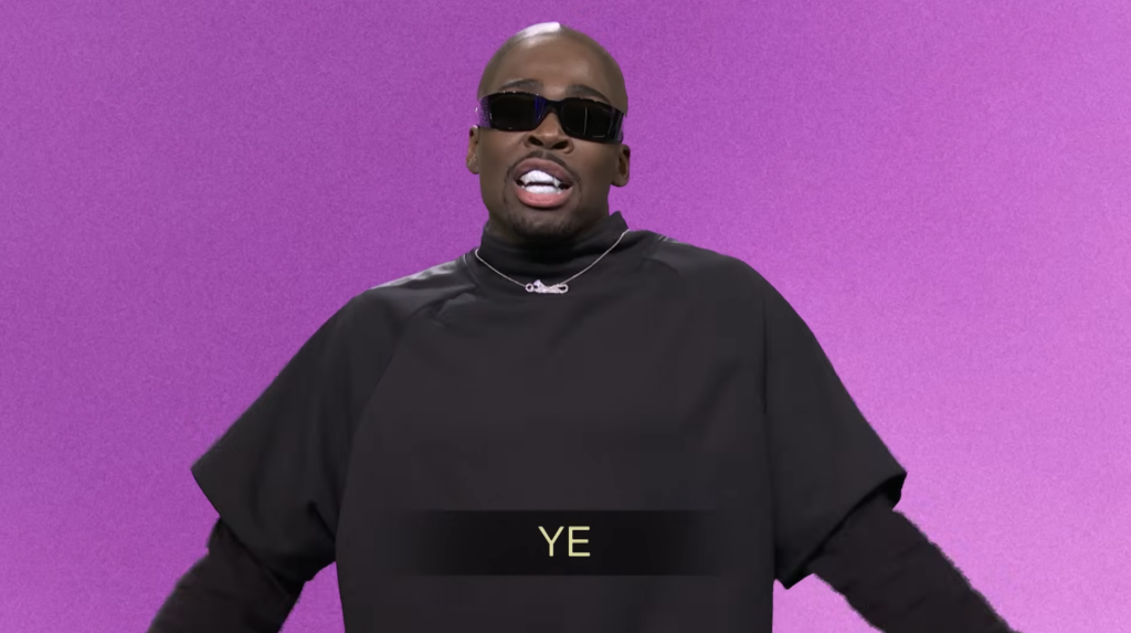 A man in a black long-sleeved shirt, black sunglasses, and a silver chain with a safety pin pendant stands against a purple background, with the word 