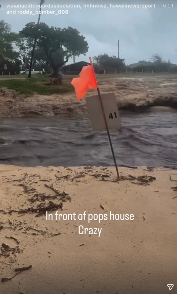 A flood of muddy water flows past a flag with the number 41 on it, with debris scattered on the sandy foreground.