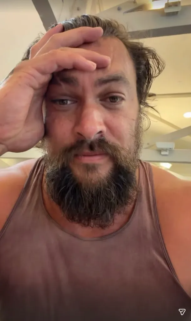 Jason Momoa looking solemn with his hand on his forehead.