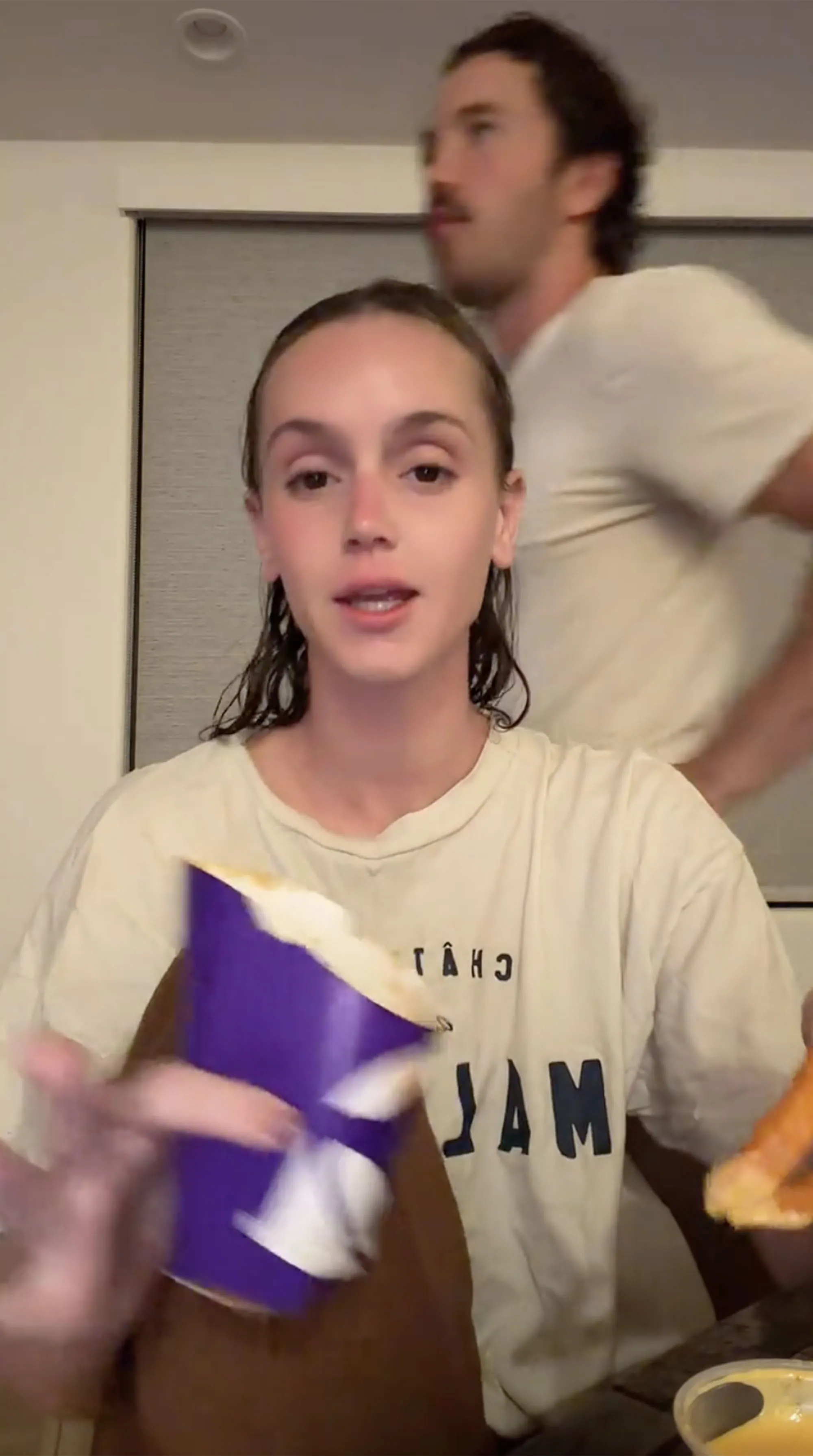 A woman holding a purple cup and a man in the background.